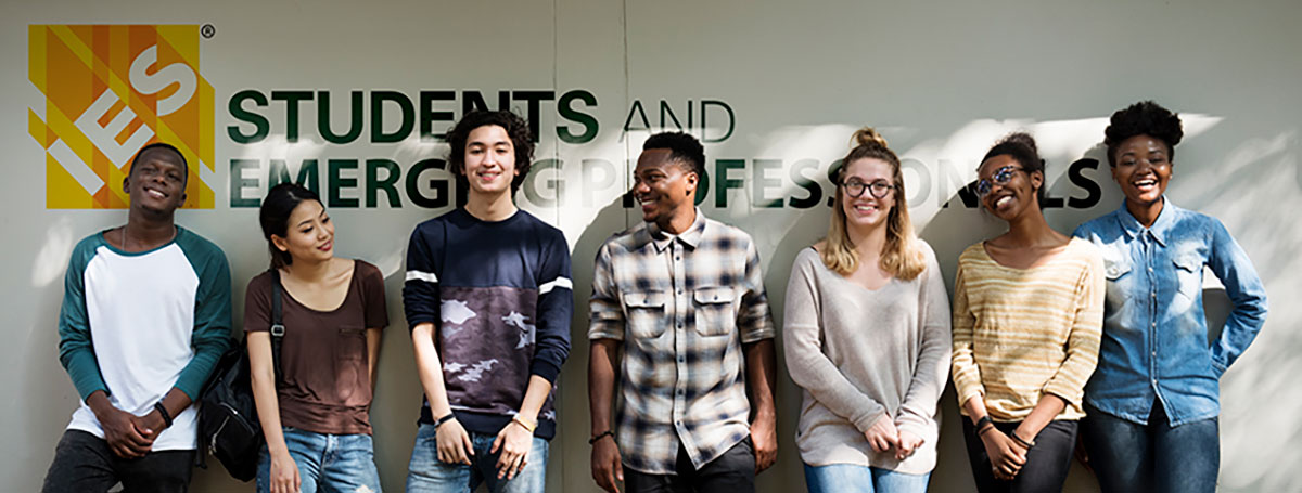 Young women and men smiling in front of a wall with the IES logo and text saying "Students and Emerging Professionals" | Students and Emerging Professionals